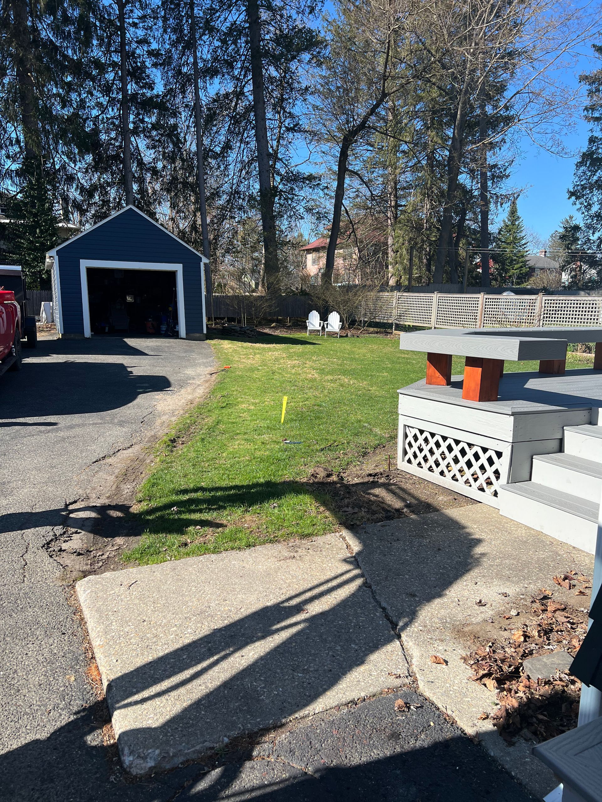 A backyard scene featuring a blue detached garage, a small patch of grass, and a gray tiered wooden deck in the foreground.