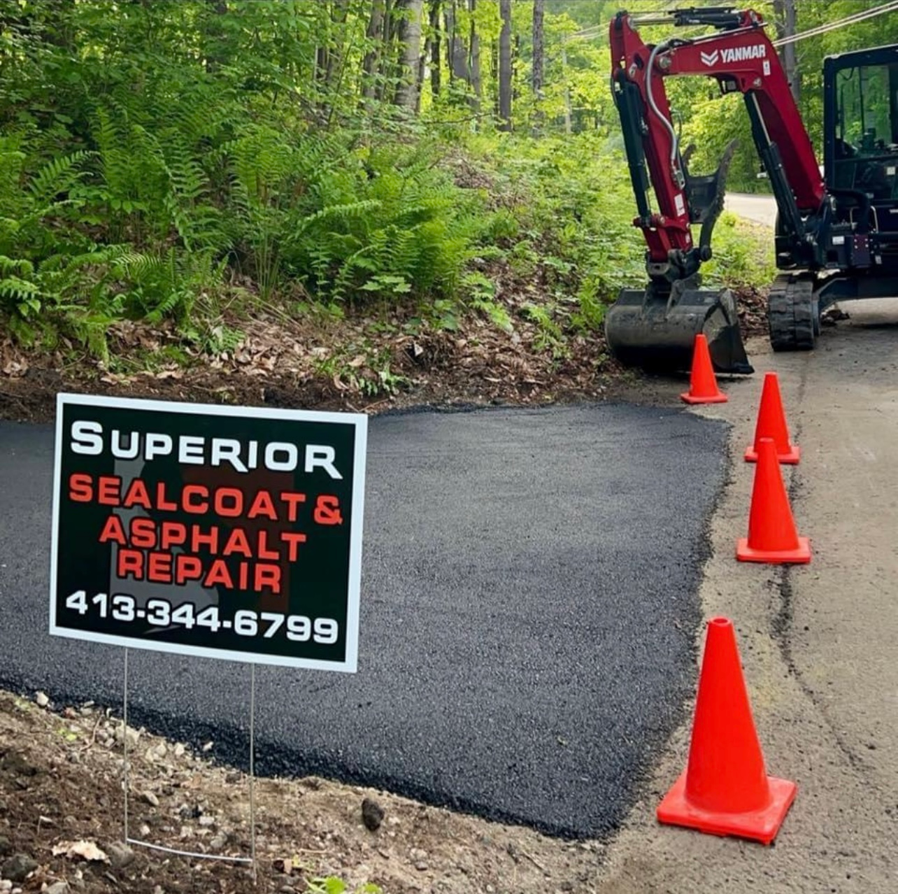A Superior Sealcoat & Asphalt Repair sign stands next to a freshly paved driveway patch with orange traffic cones.