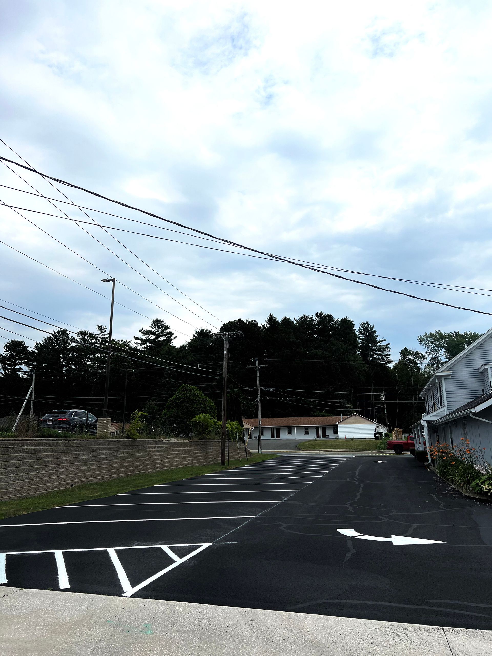 A newly paved parking lot with white painted markings and directional arrows under a cloudy, overcast sky.
