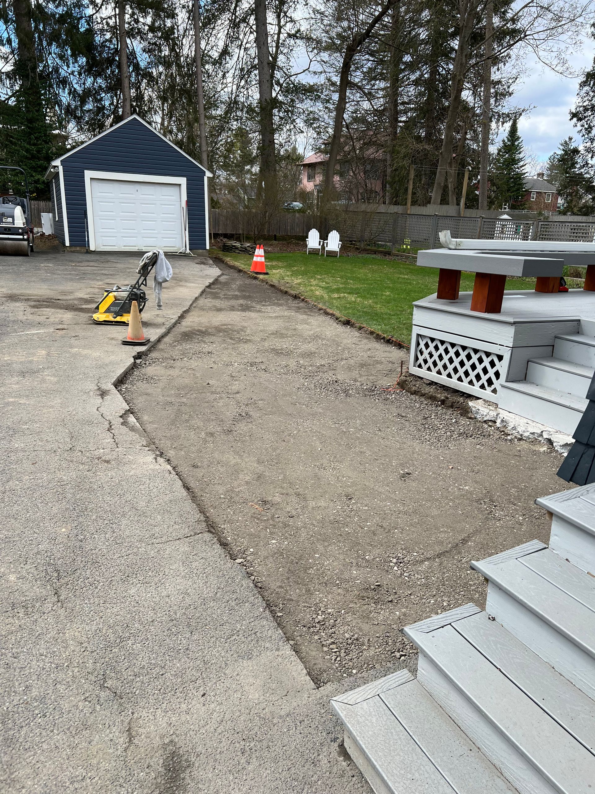 A gravel walkway leading toward a detached blue garage and a wooden deck with white stairs.