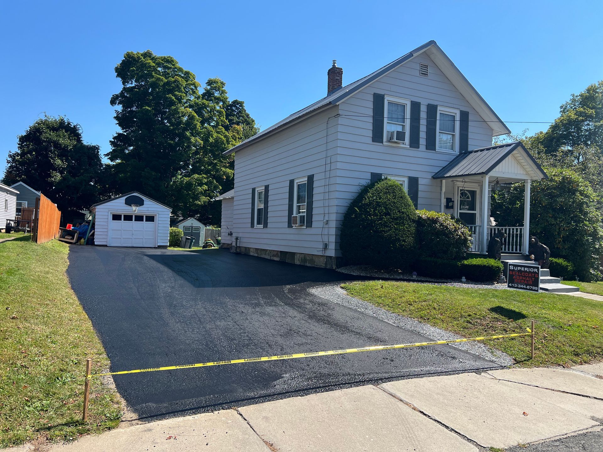 A white two-story house with a newly paved asphalt driveway and a detached garage on a sunny day.