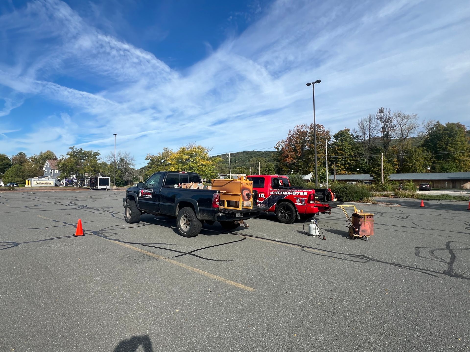 A dark pickup truck towing a generator and a red truck parked in a large asphalt lot on a sunny day.