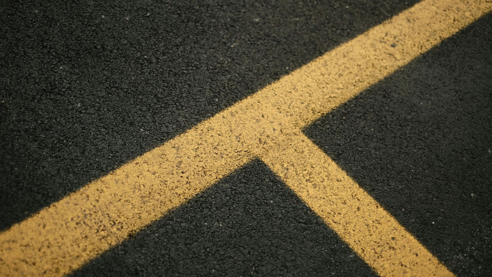 Two yellow lines intersecting at an angle on a dark gray asphalt surface.