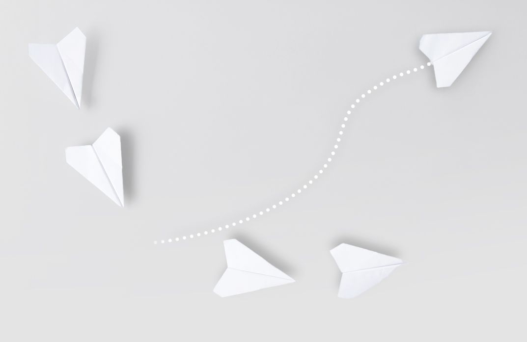 A group of paper airplanes flying in opposite directions on a gray background.