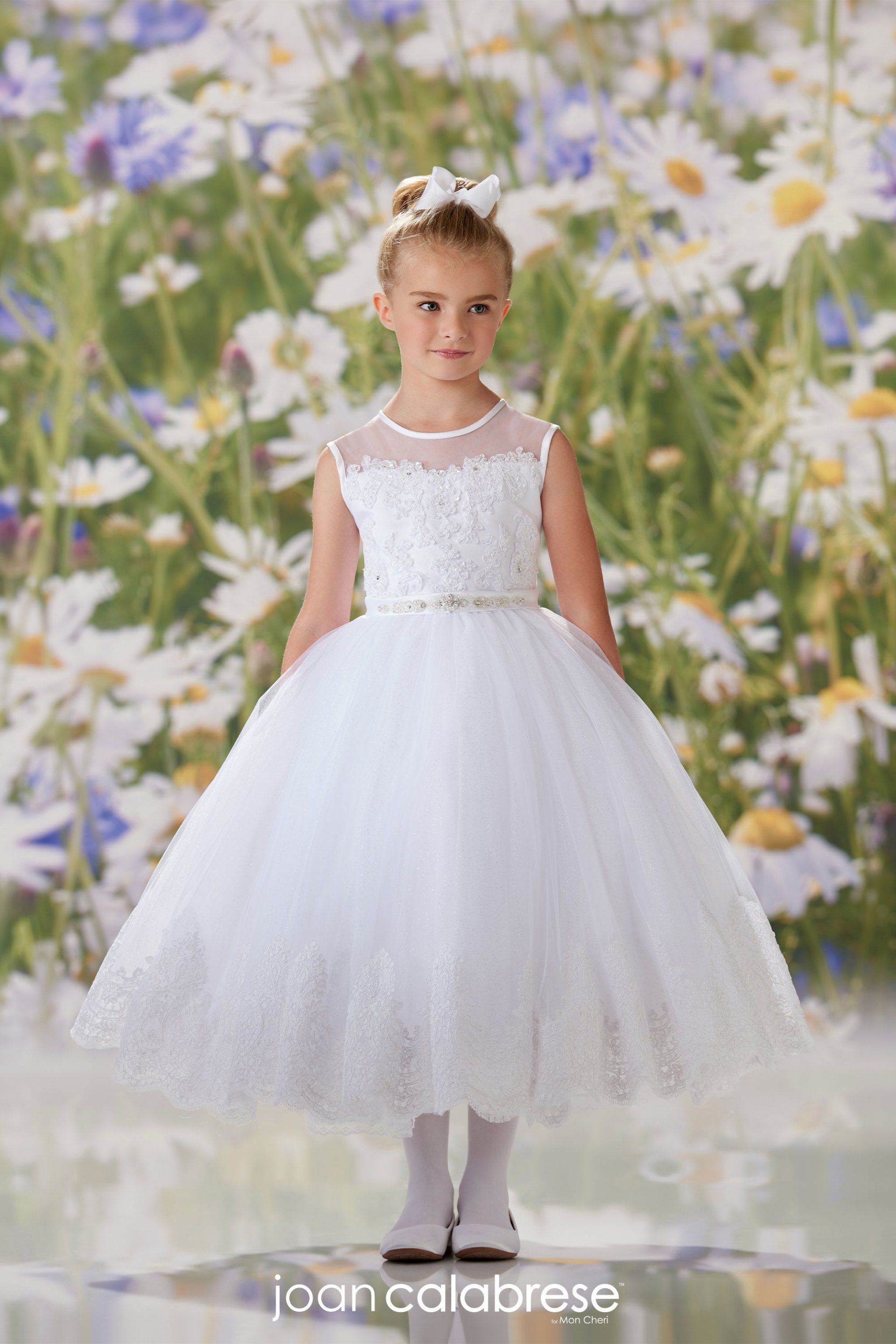 Young girl in a white tulle dress standing before a floral backdrop