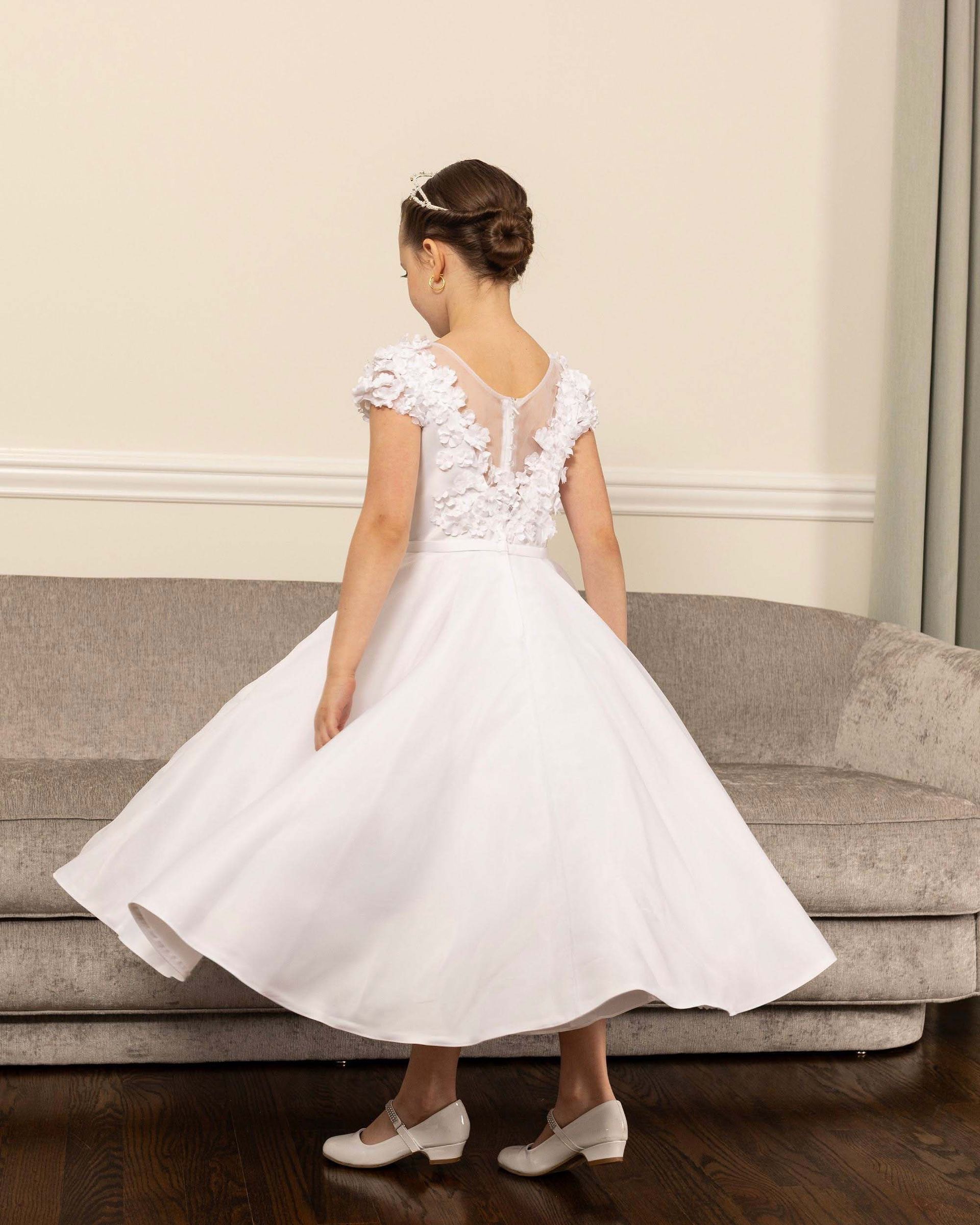 Young child in a white dress twirling in a living room, seen from behind