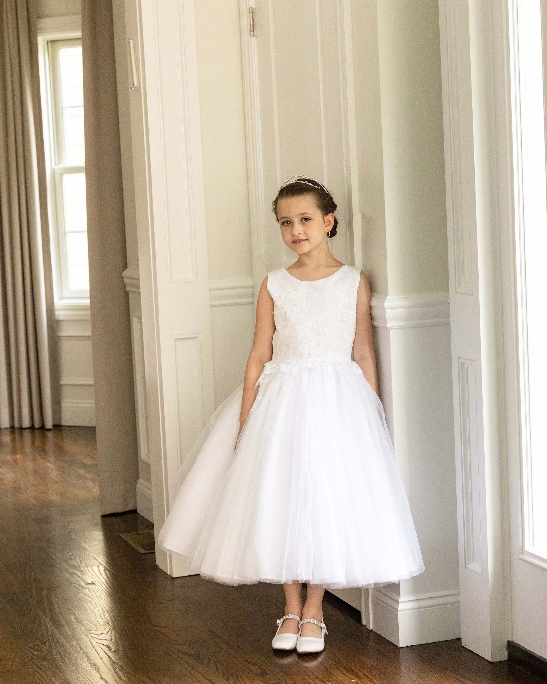 Young girl in a white dress standing by tall windows in a bright hallway
