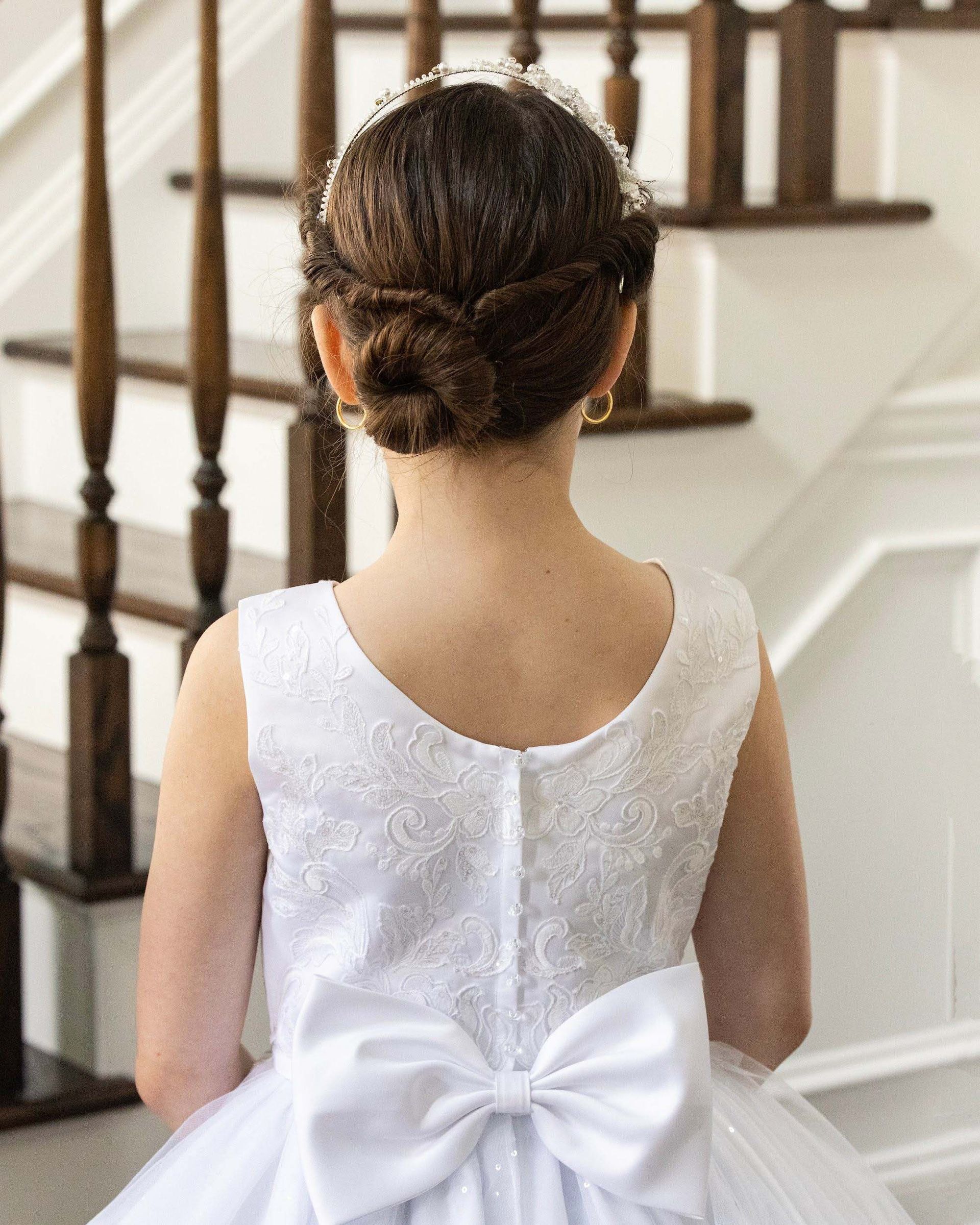 Child in a white dress with a large bow on the back, viewed from behind on a staircase.