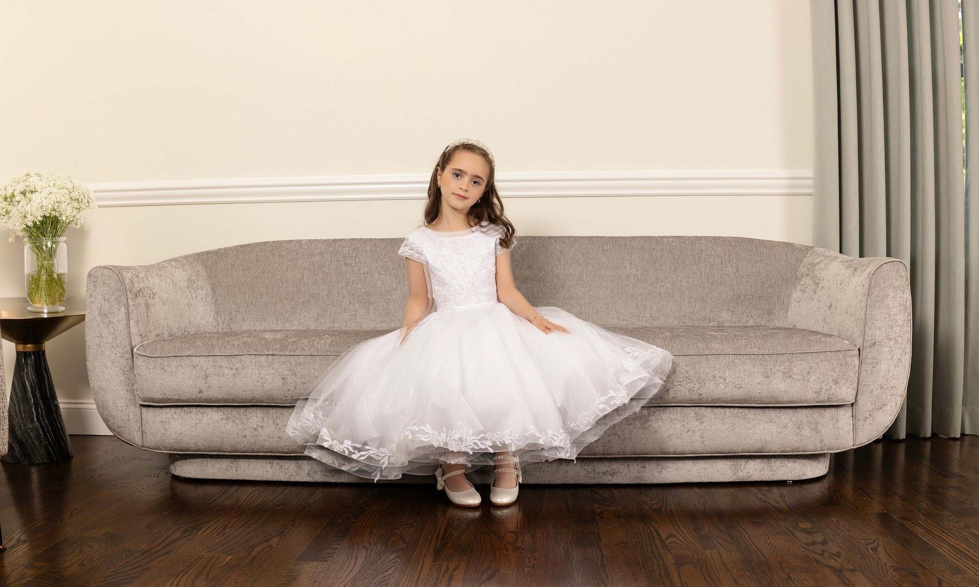 Young girl in a white dress sitting on a couch in a bright living room