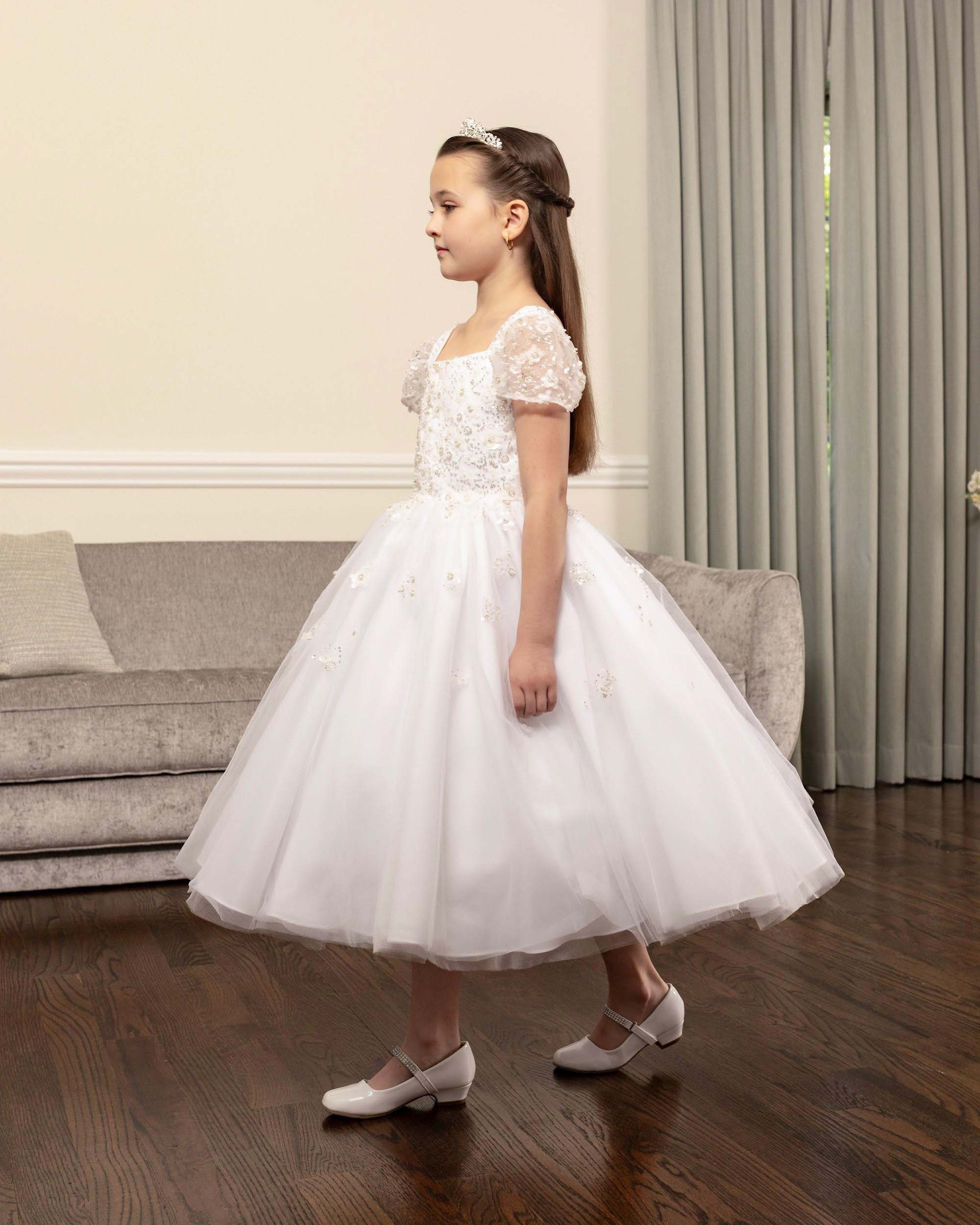 Young girl in a white dress and shoes standing in a living room, side view