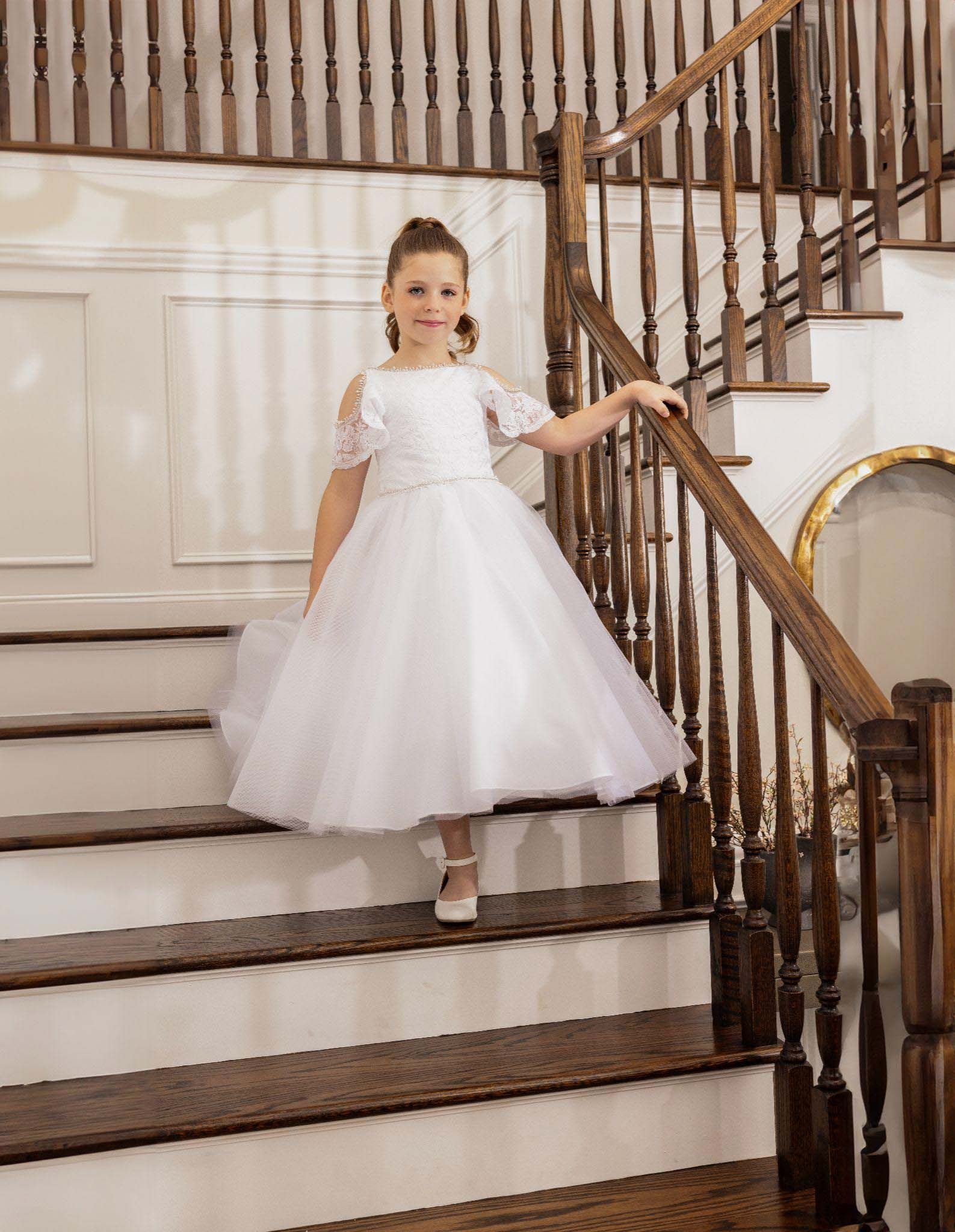 Young girl in a white dress standing on a staircase in a bright home interior