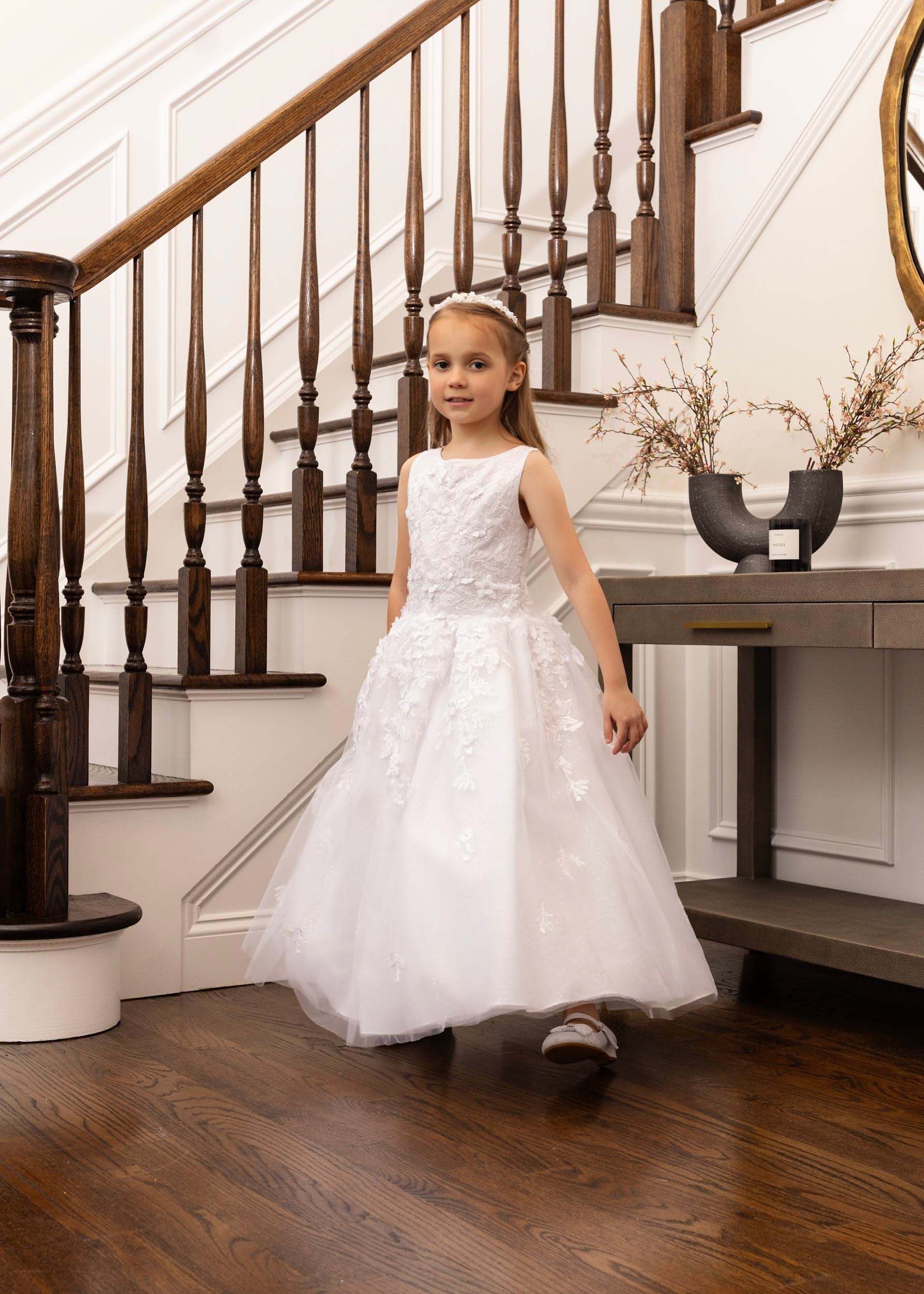 Young child in a white dress standing in a staircase foyer beside a fireplace