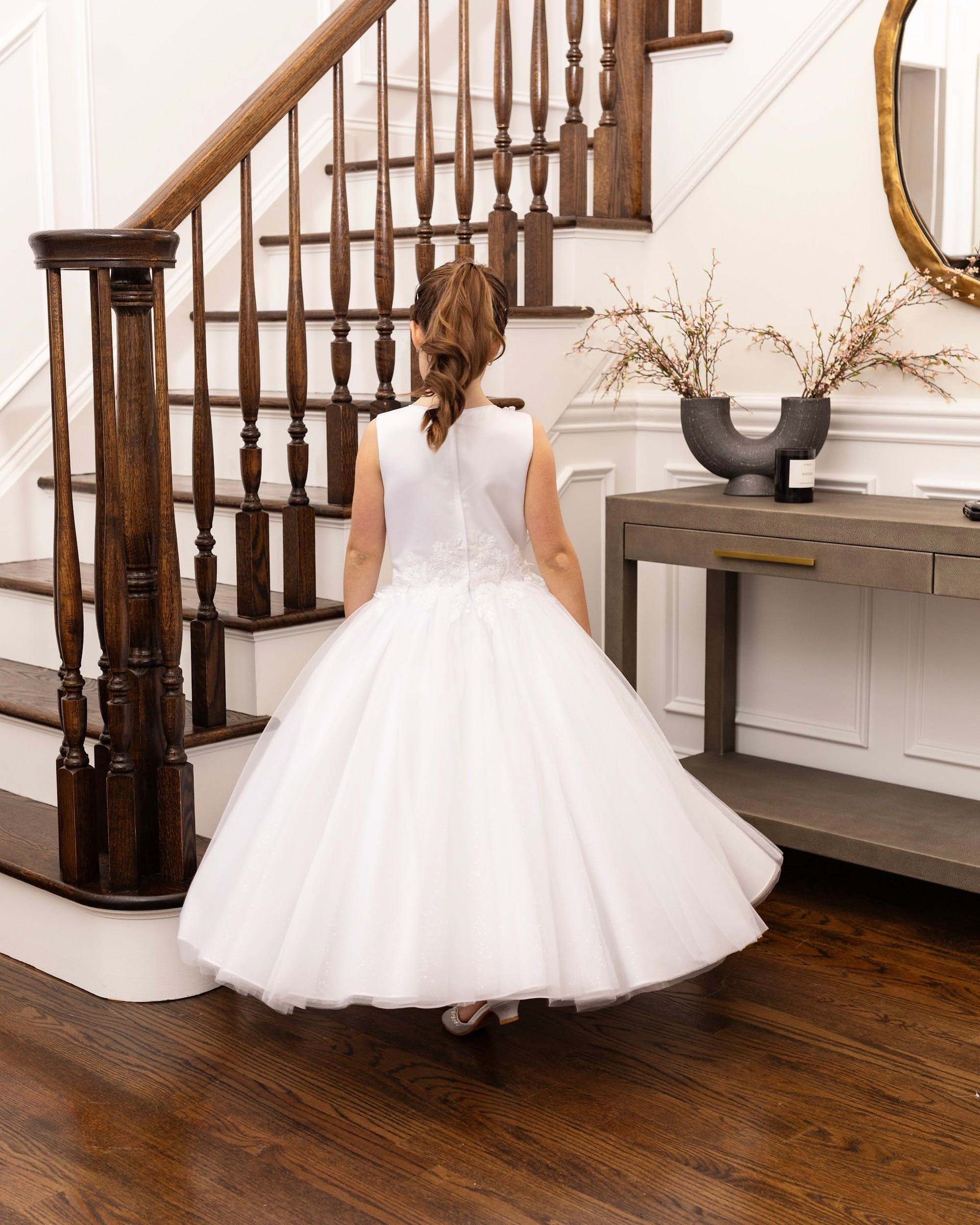 Child in a white dress standing by a staircase in a bright home interior