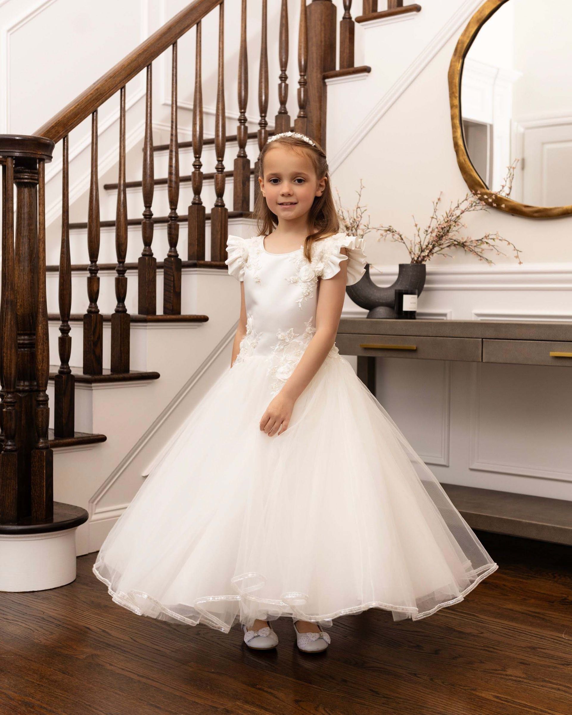 Young girl in a white dress standing on a staircase landing beside a console table and round mirror