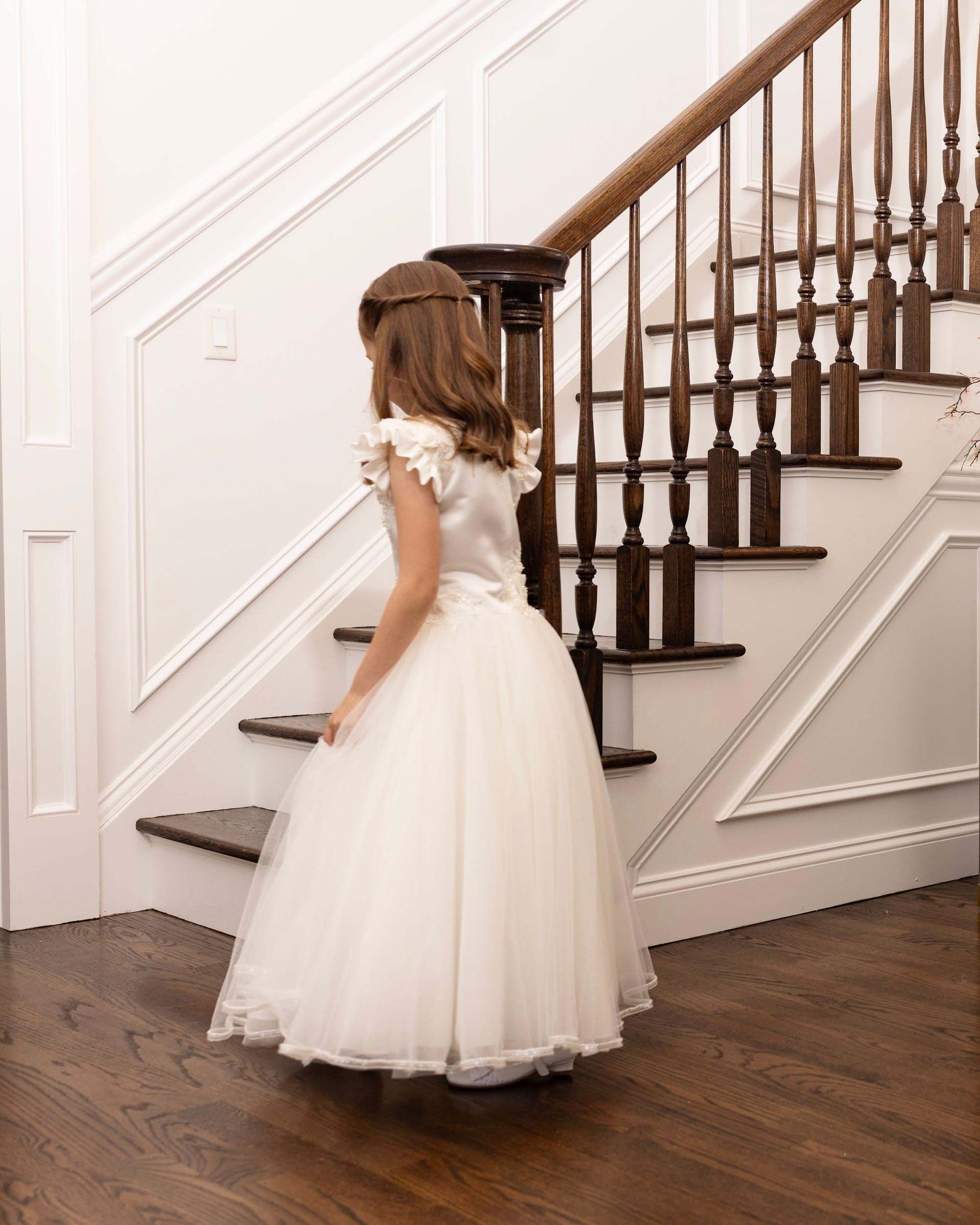 Young child in a white dress standing on a staircase in a bright interior hallway