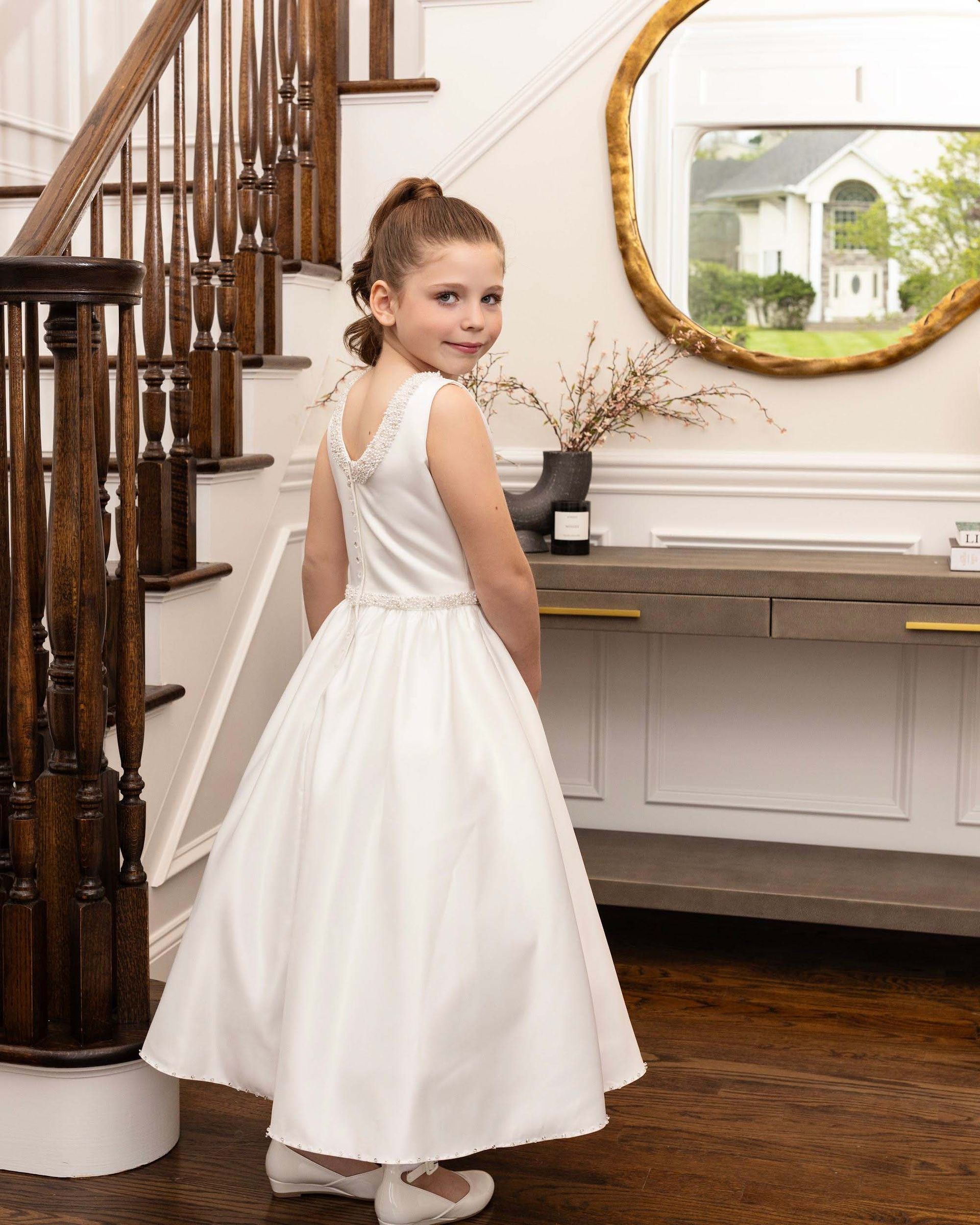 Young girl in a white dress turning on a staircase in a bright room