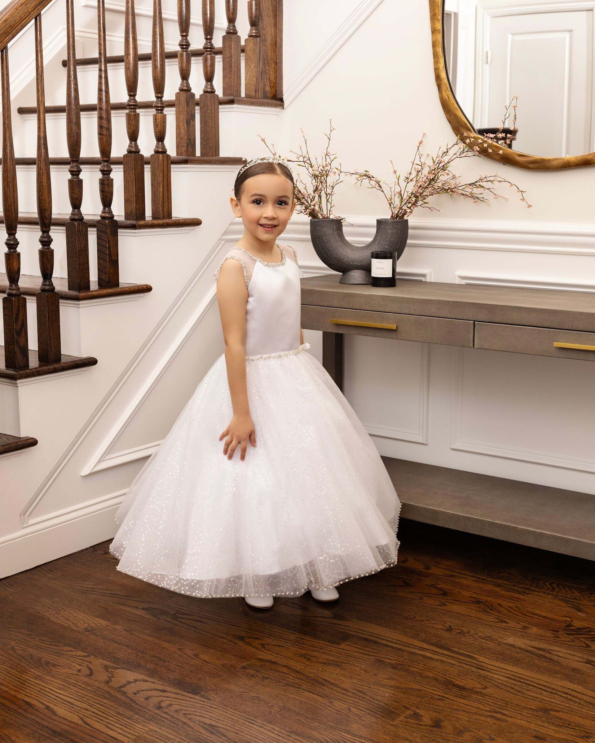 Young child in a white dress standing by a staircase in a decorated room