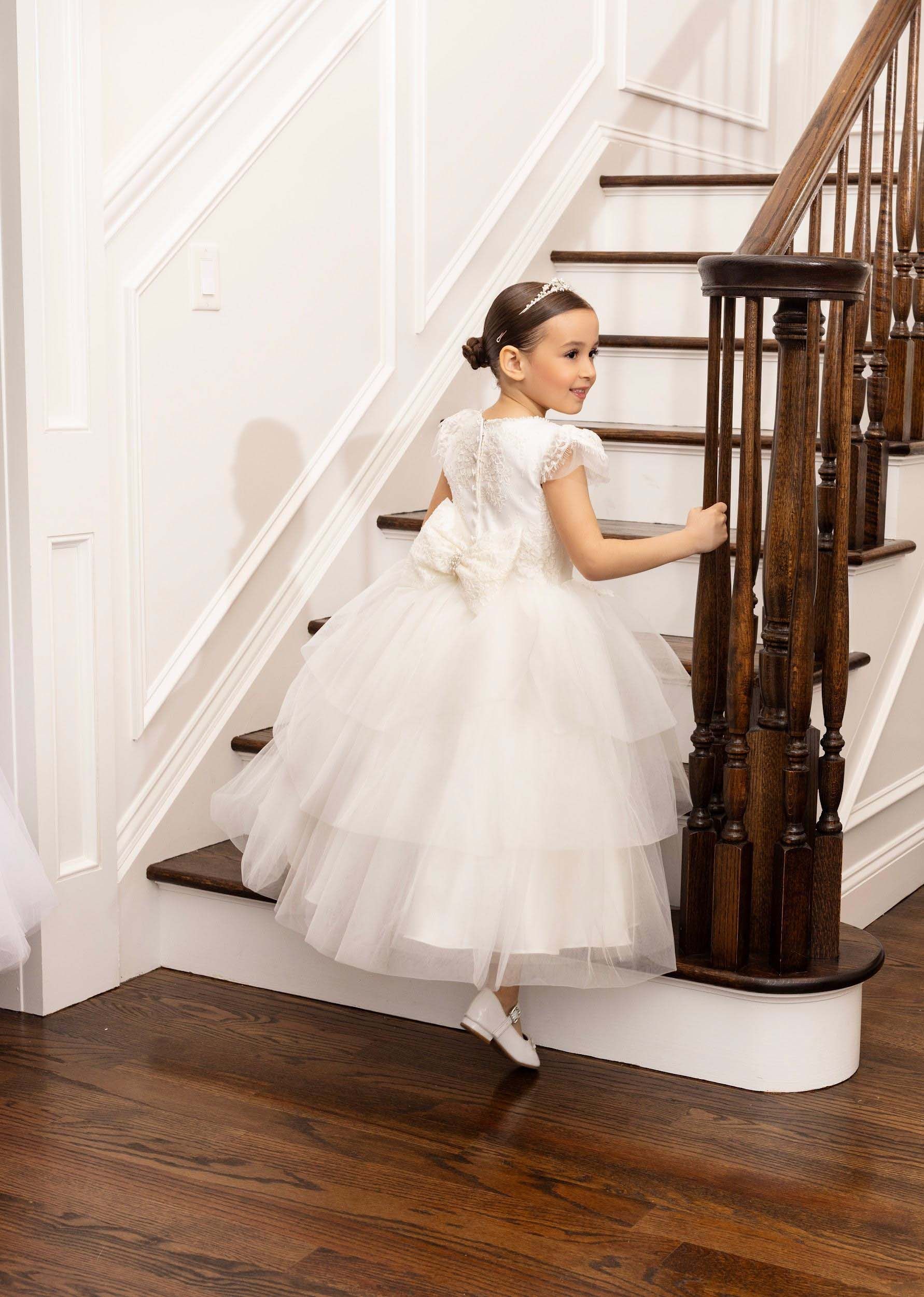 Child in a white dress climbing a staircase with a dark wooden banister in a bright home interior