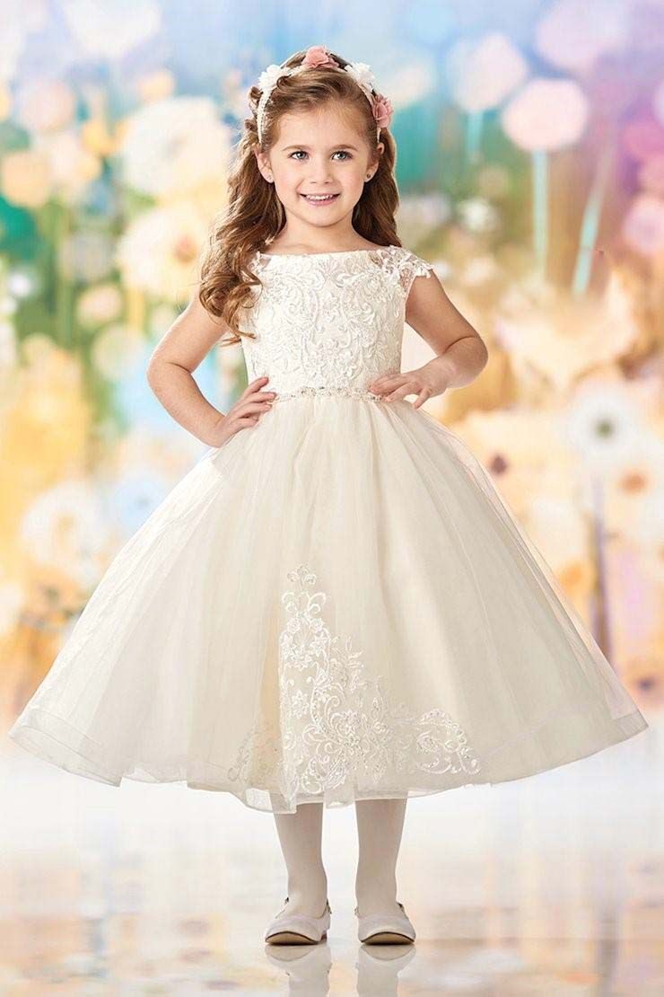 Young girl in a white lace dress standing against a pastel, softly blurred backdrop