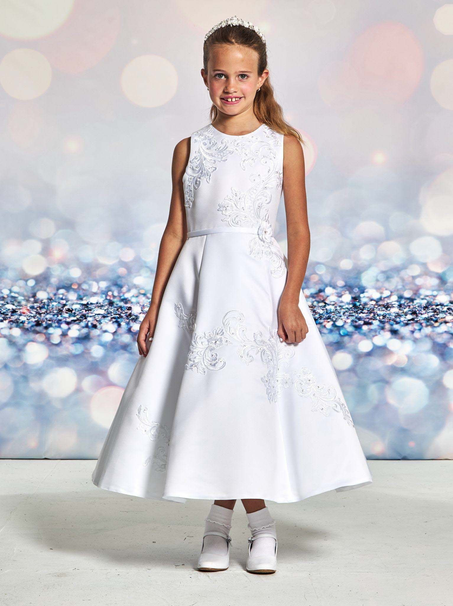 Girl in a white dress and white shoes standing against a sparkling bokeh backdrop.