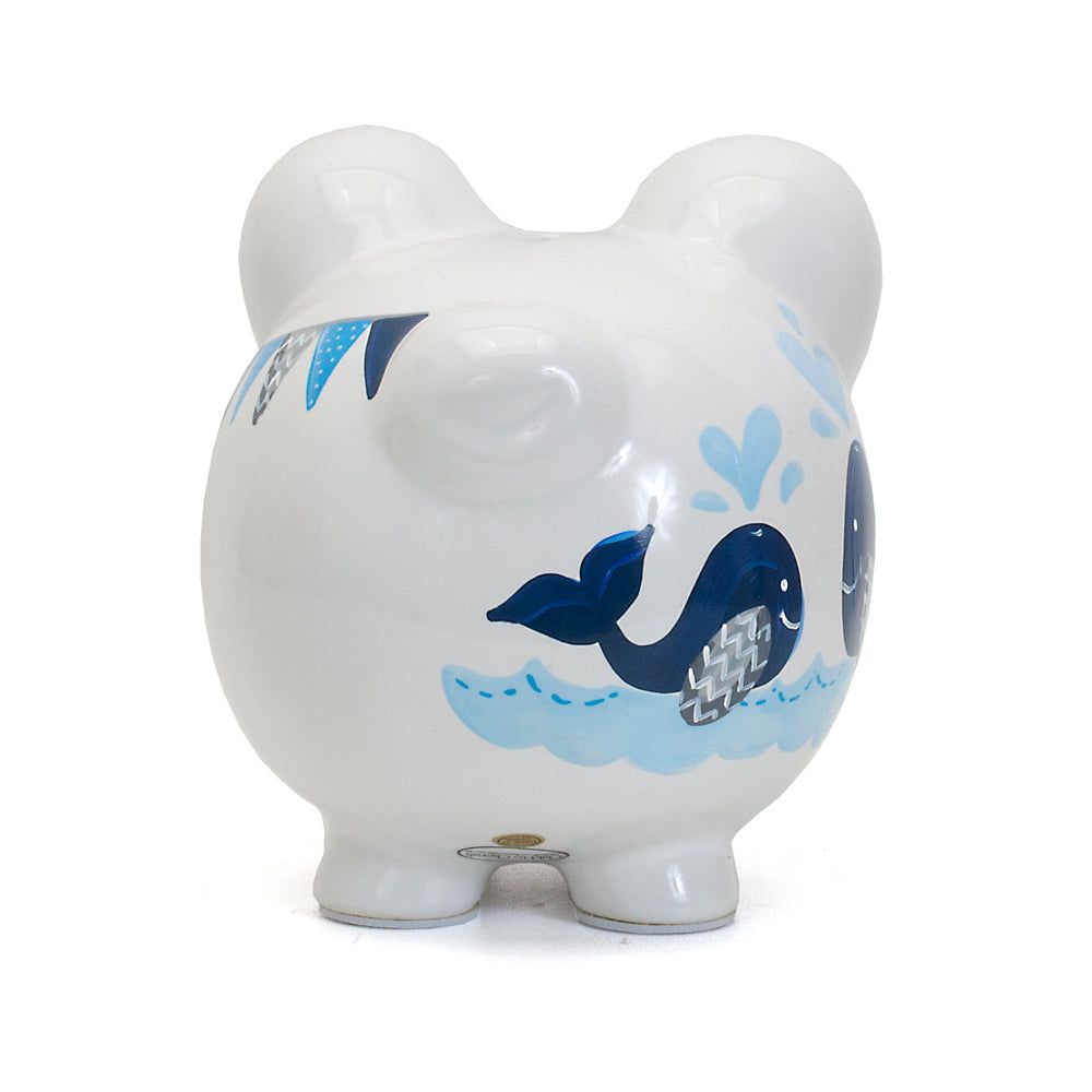 White ceramic piggy bank with blue whale and wave design on a plain background