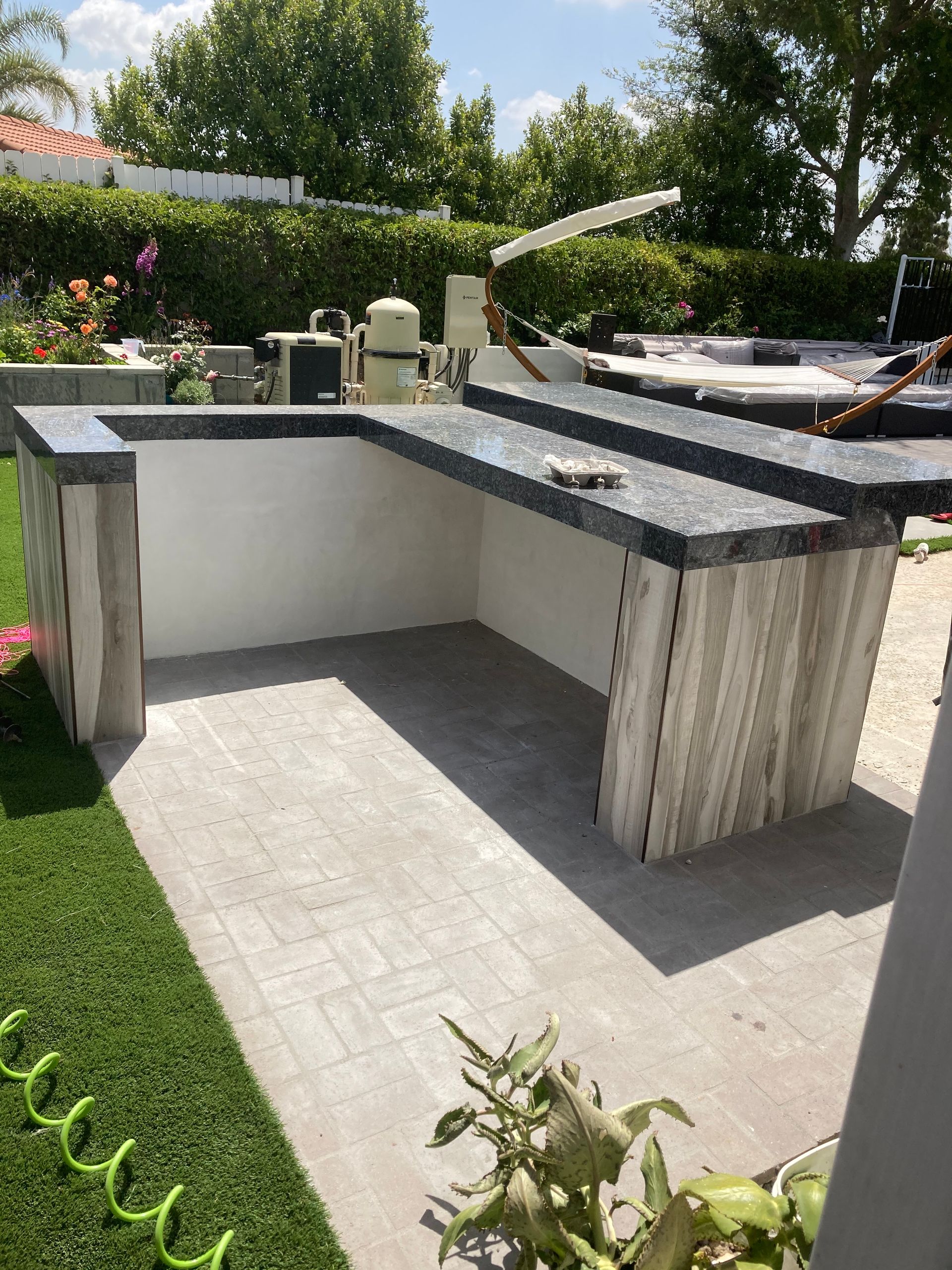 Outdoor backyard kitchen with stone counter and built-in grill beside a patio and lawn.