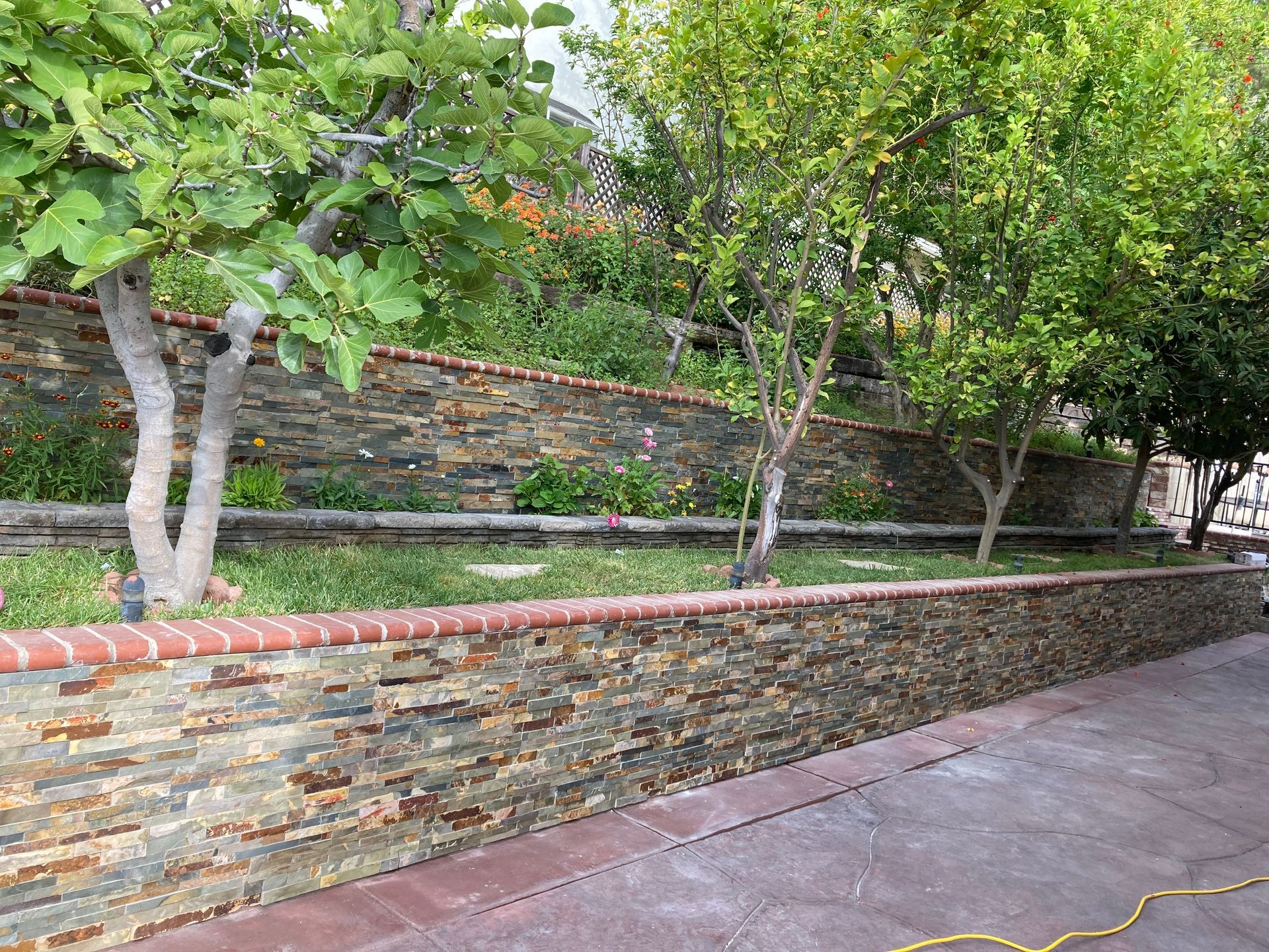 Stone retaining wall beside a tree-lined path with grass and a wet walkway.
