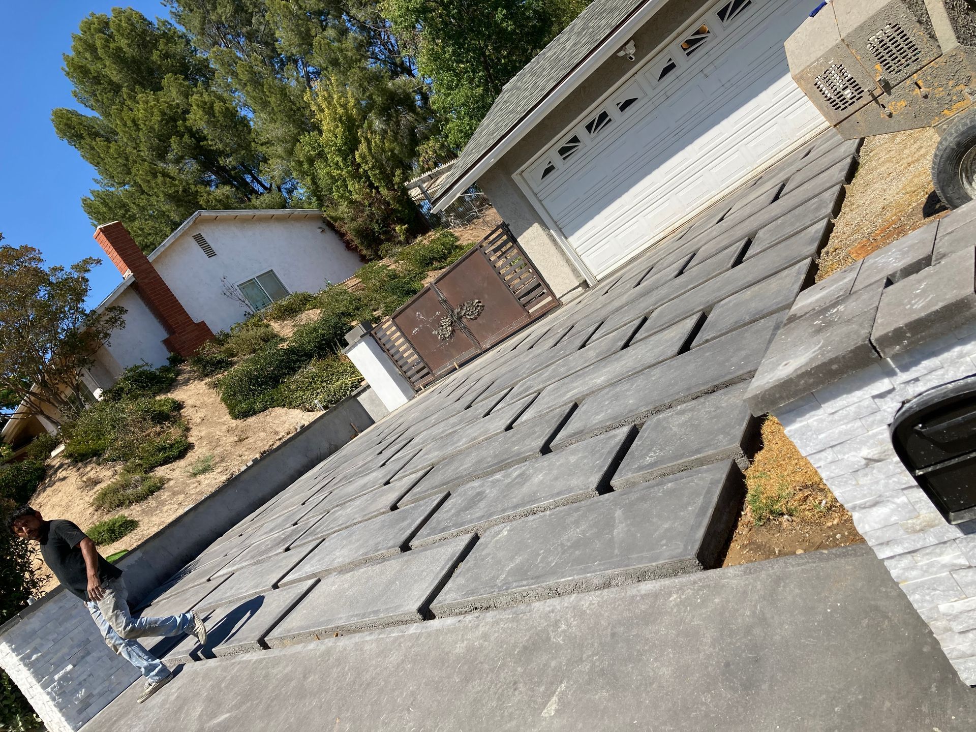 Sloped driveway with dark pavers leading to a white garage, with a person standing at the left edge.