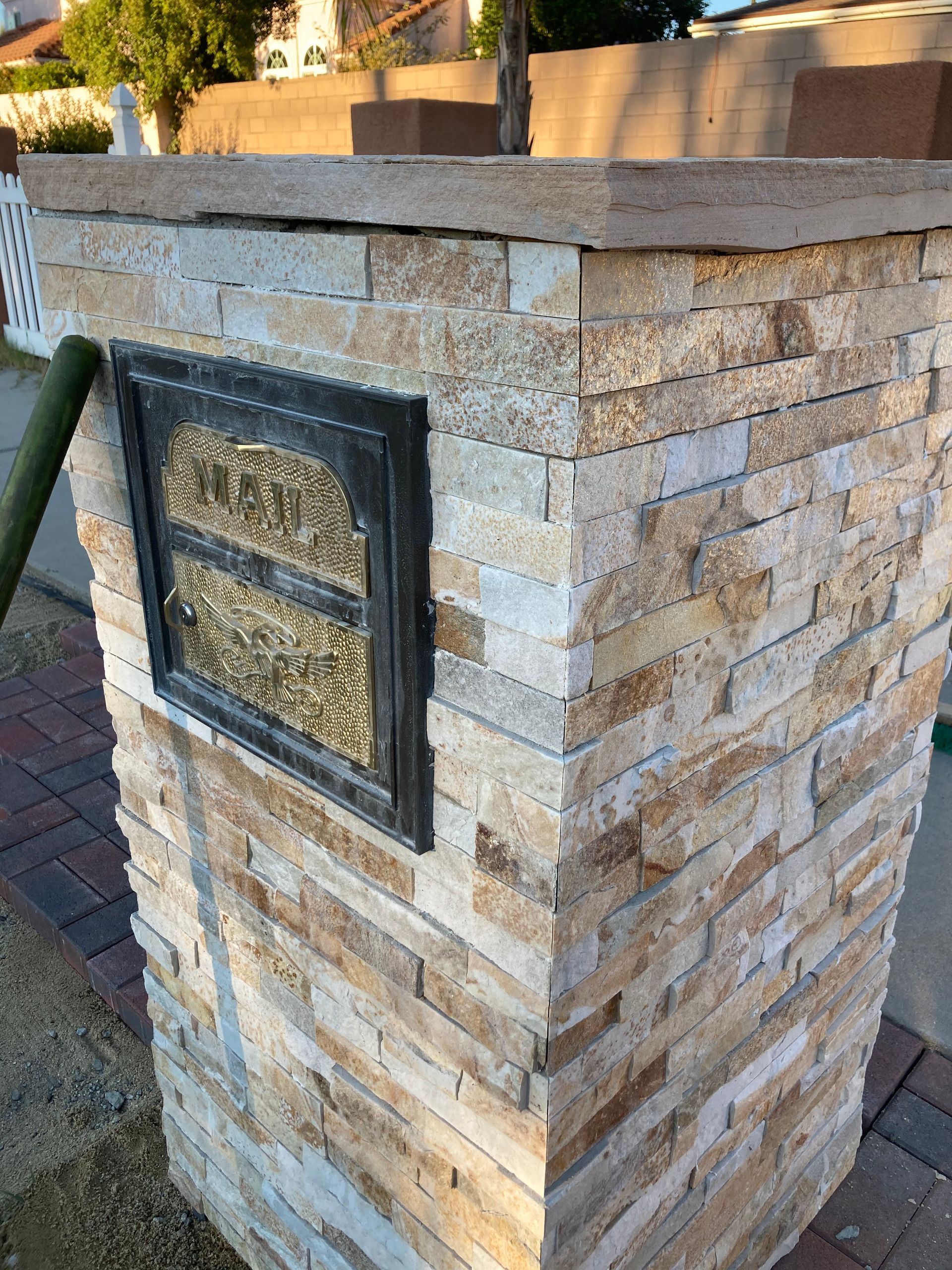 Stone pillar with a black-framed plaque and a dark cap, outdoors by a path.