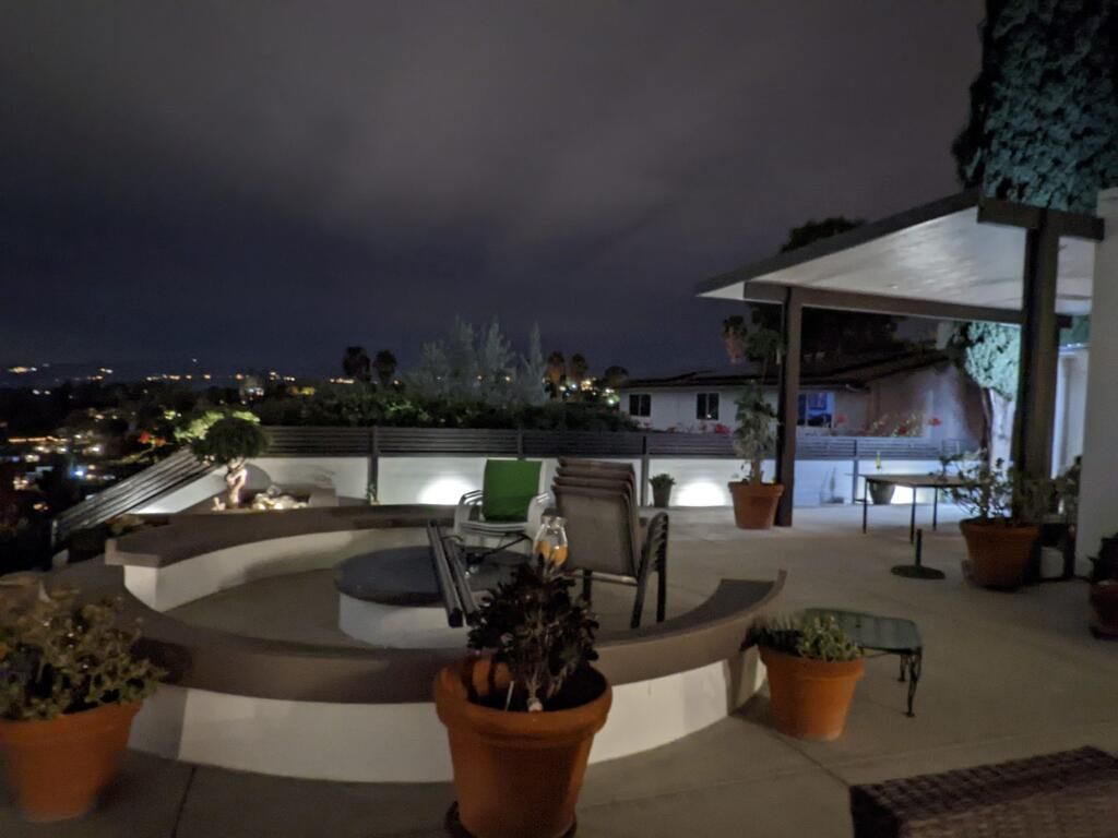 Rooftop patio at night with potted plants, lounge chairs, and city lights in the distance