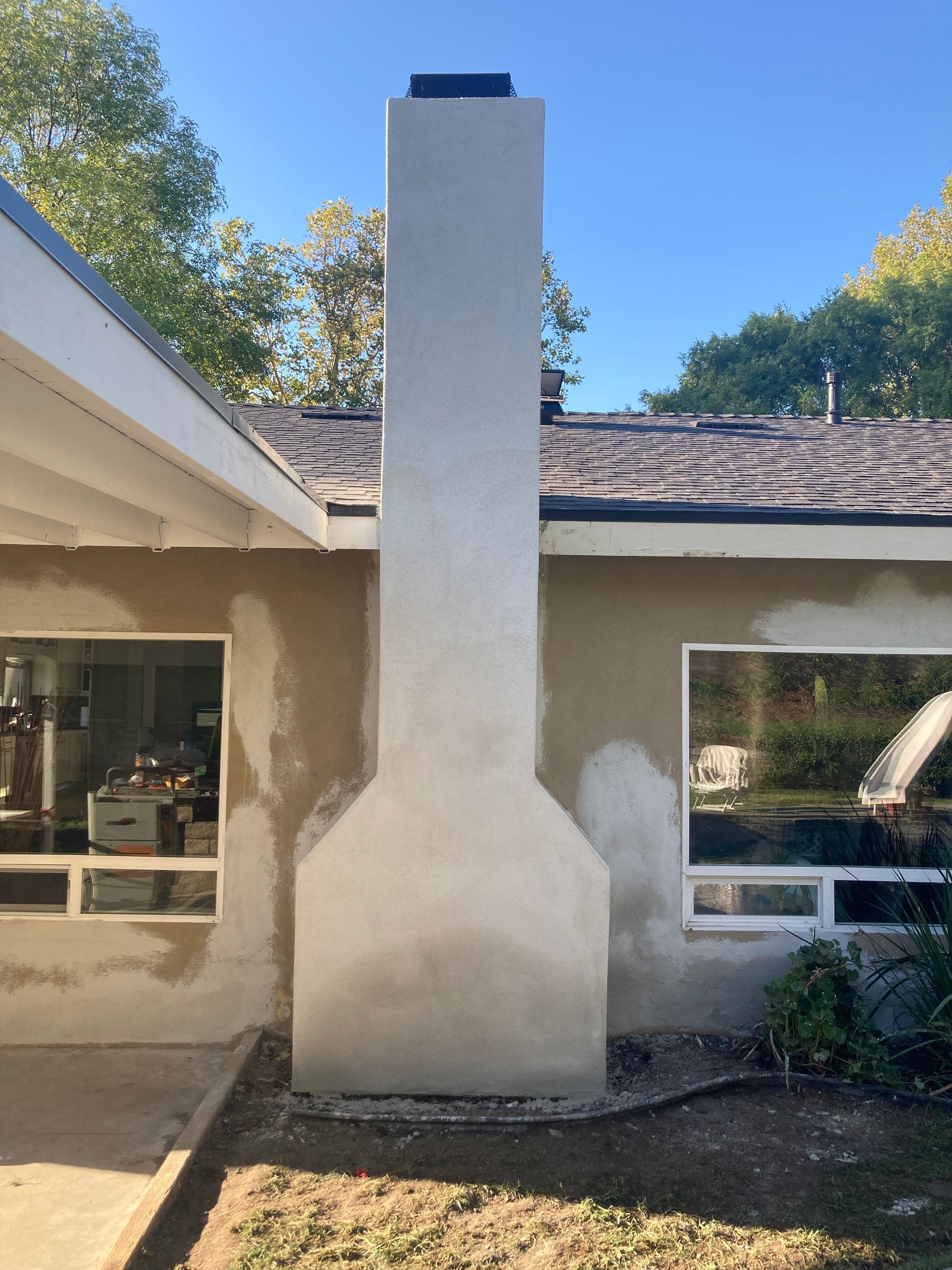 Stucco chimney centered on a single-story house with white trim and a shingled roof.