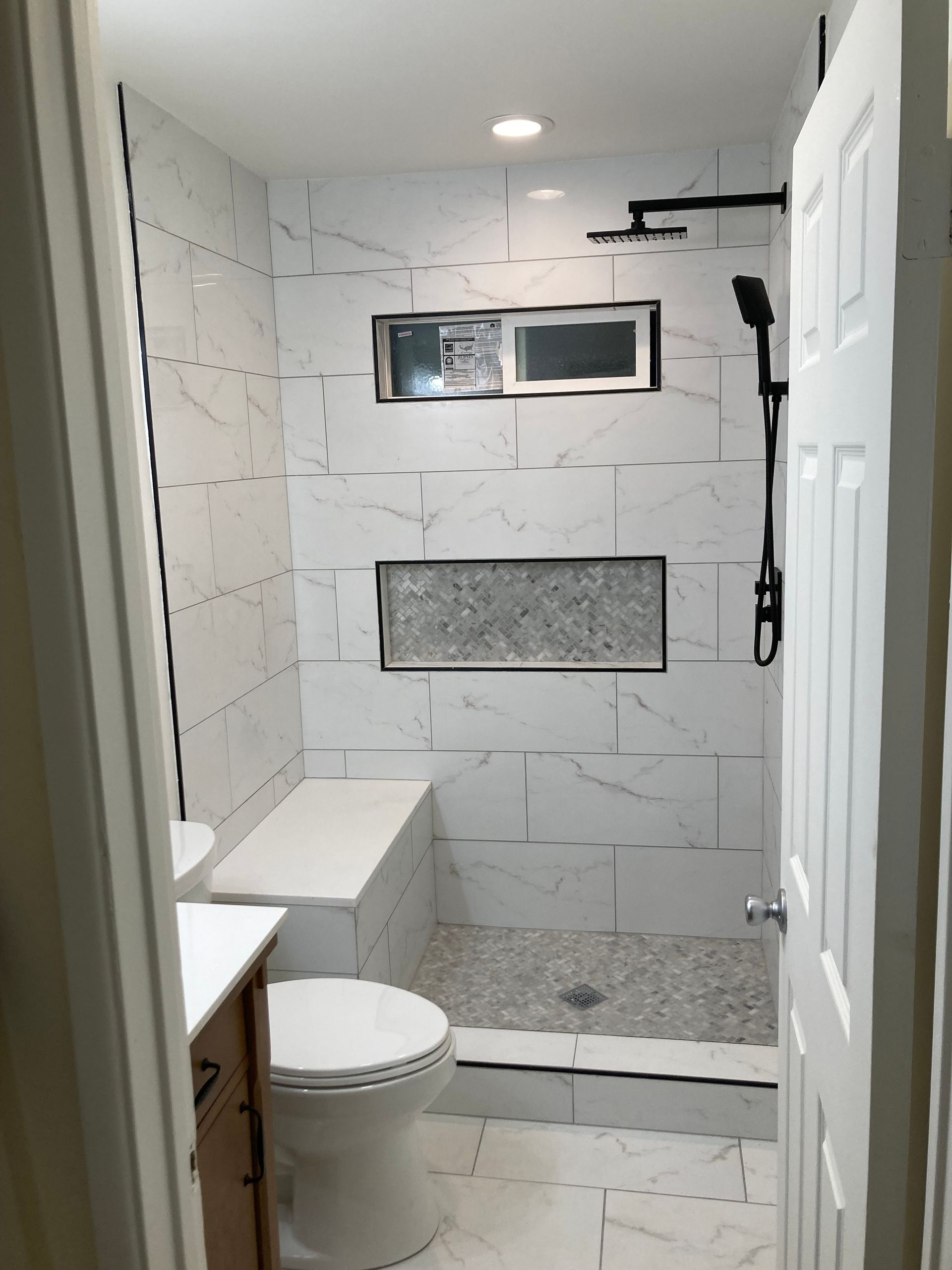 Small tiled bathroom with toilet, shower, and a window on the back wall.