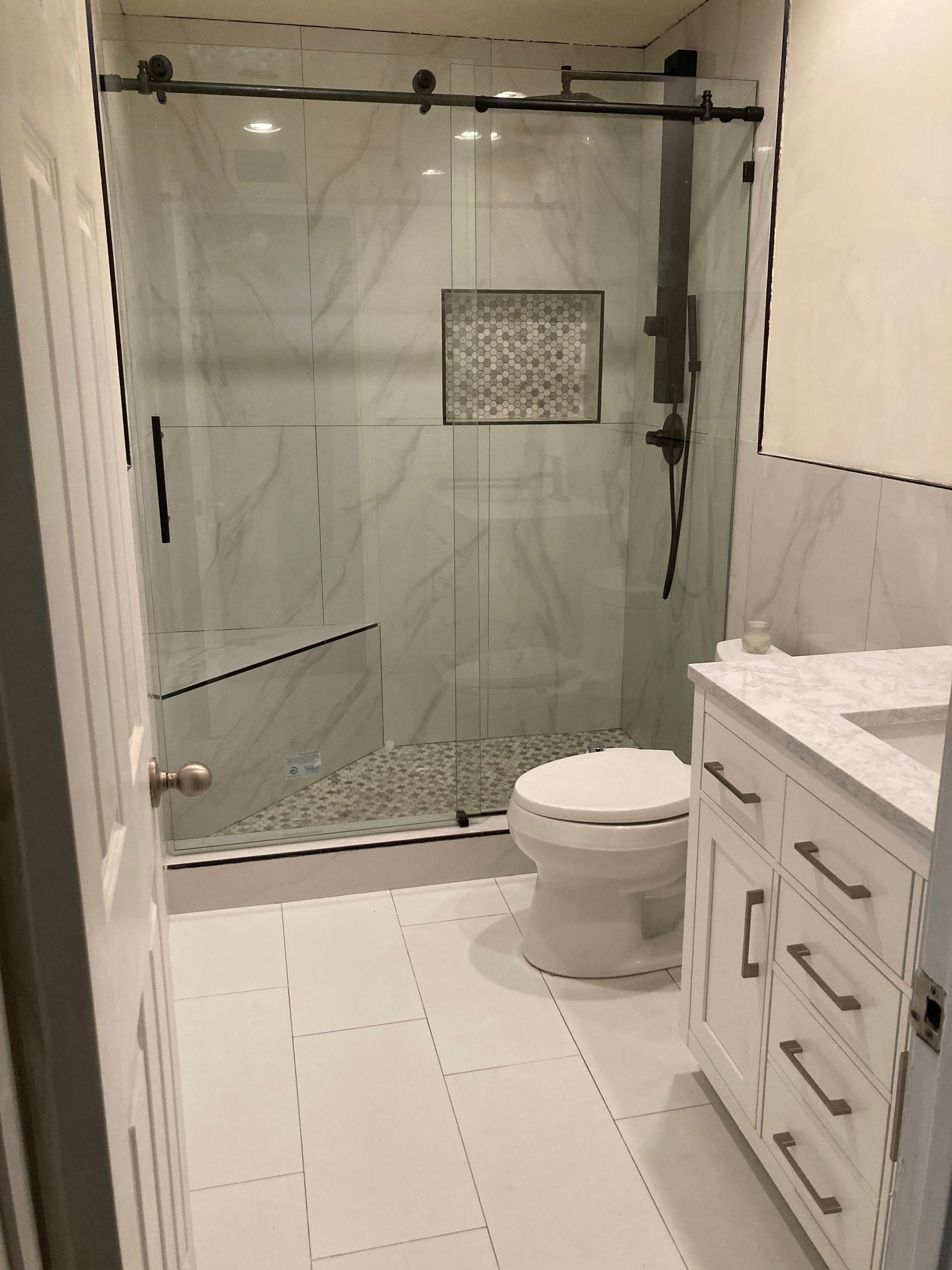 Modern bathroom with glass shower, toilet, and white vanity on tiled floor