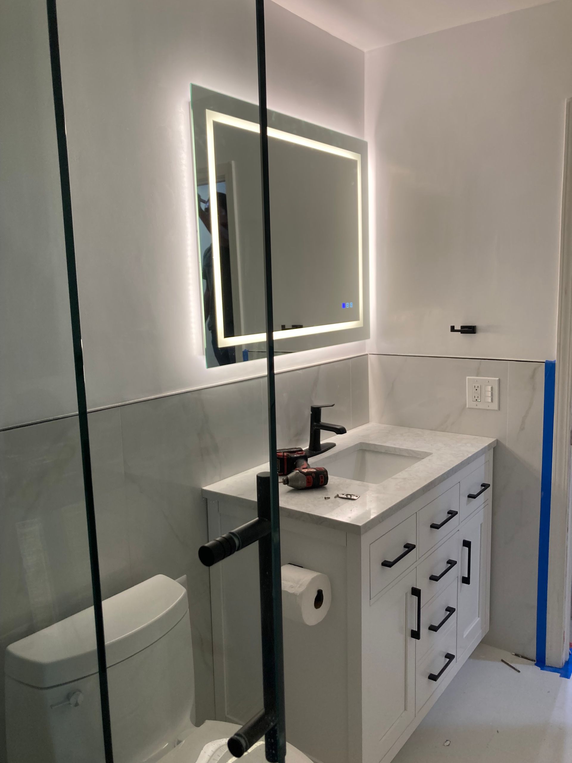 Small modern bathroom with glass shower, lit mirror, white vanity, and toilet.