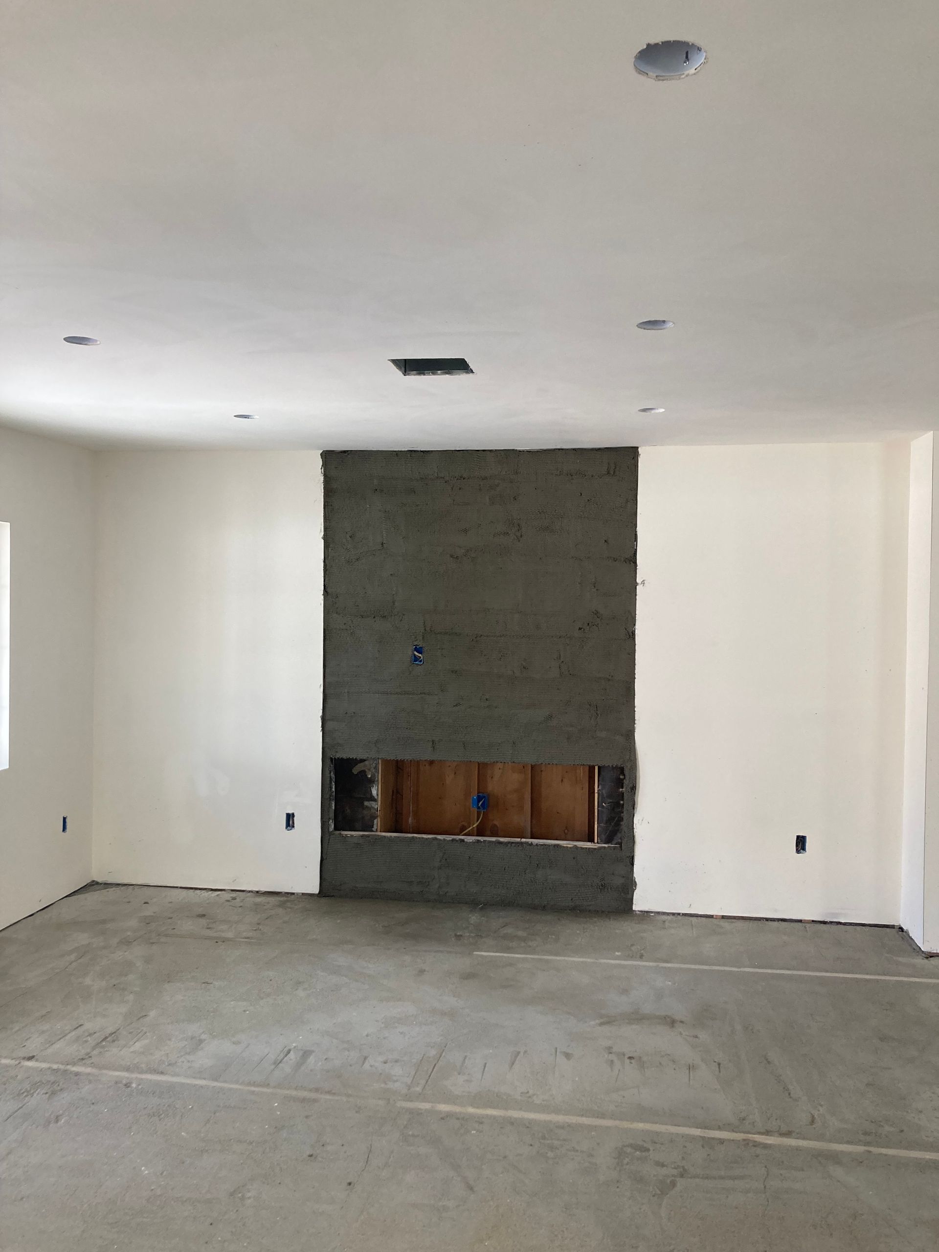 Empty unfinished room with white walls, concrete floor, recessed ceiling lights, and a central fireplace surround