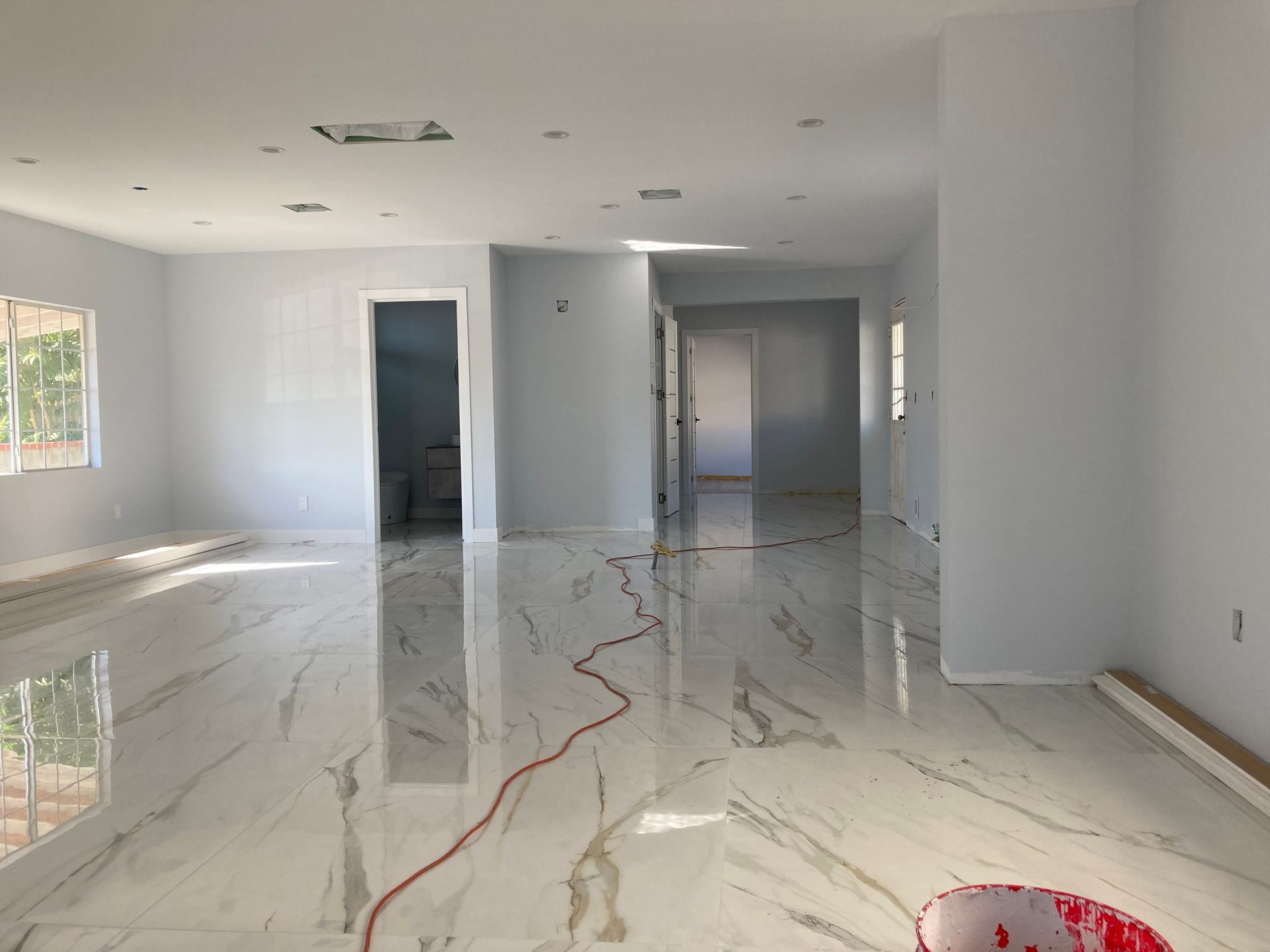 Empty bright room with glossy white marble floors, gray walls, and doorways in the back