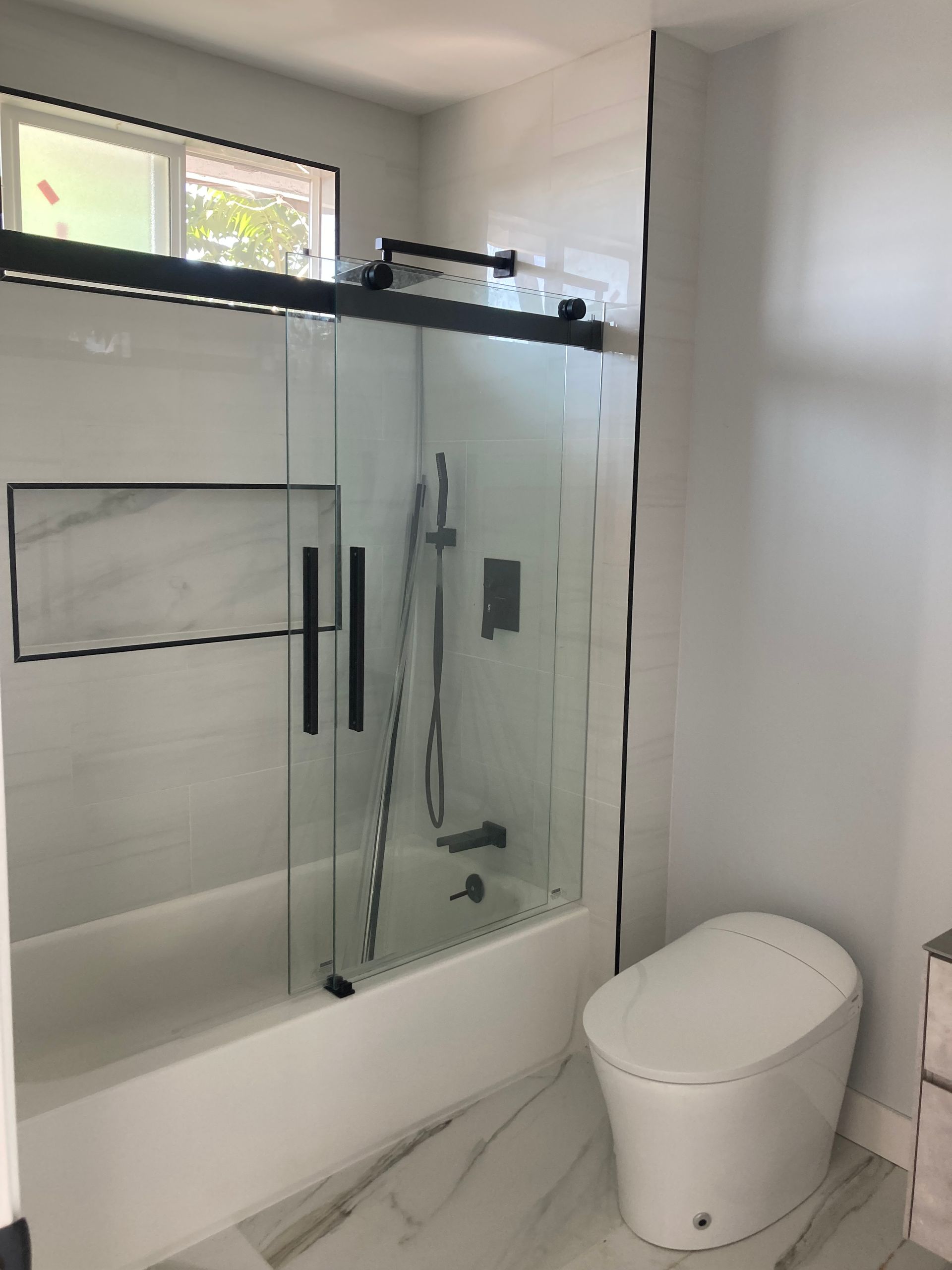 Modern bathroom with glass shower enclosure, white tile, and a white toilet beside the shower