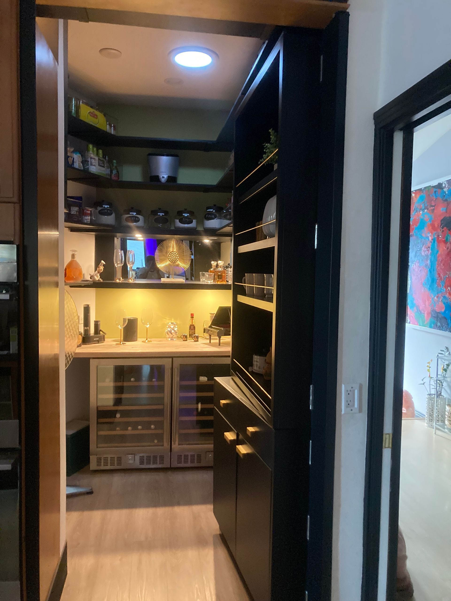 Narrow hallway leads to a warmly lit pantry with shelves, cabinets, and a small wine fridge.