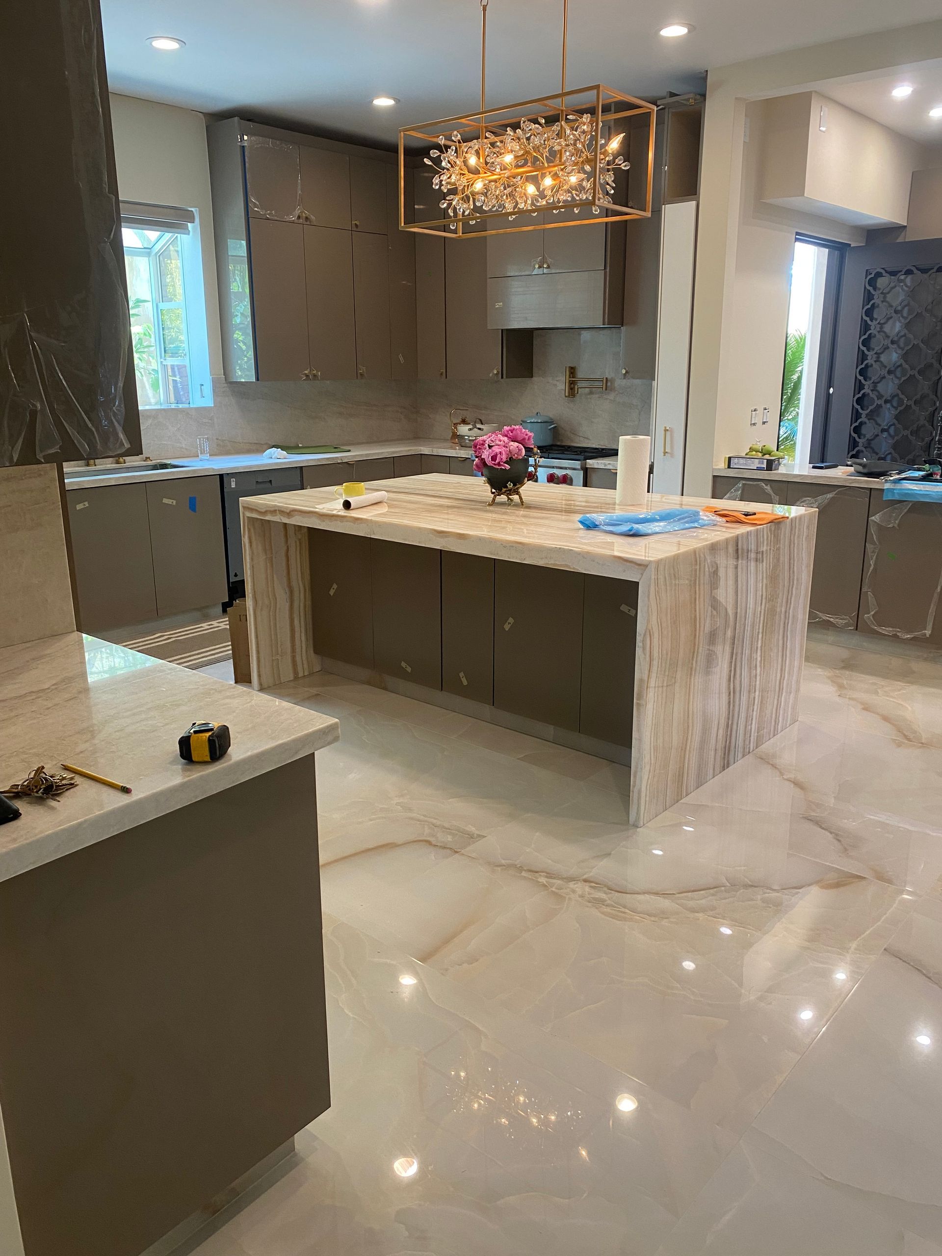 Modern kitchen with marble island, pendant light, and glossy tiled floor; bright, spacious interior.