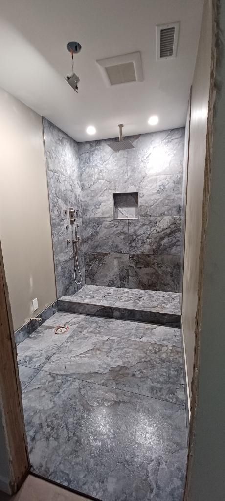 Small unfinished tiled shower room with stone-pattern walls, bench, and recessed niche under ceiling lights