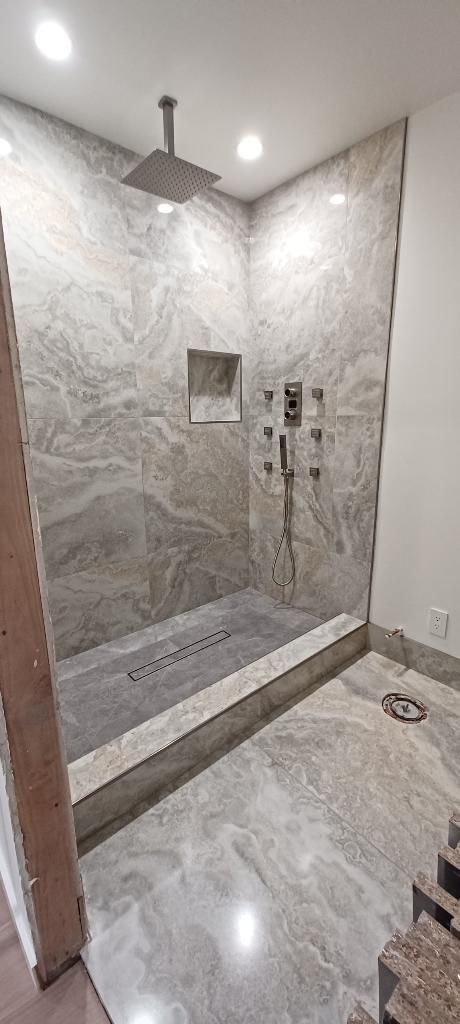Marble-tiled walk-in shower with rainfall showerhead, bench, and glass partition in a bright bathroom