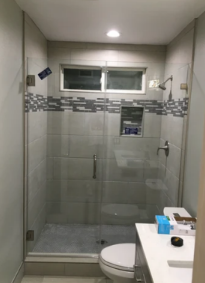 Small bathroom with glass shower stall, toilet, and sink, seen from the doorway.