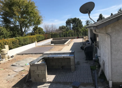 Rooftop patio with pavers, low walls, a satellite dish, and surrounding trees under a clear sky.