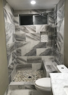 Small tiled bathroom with shower, window, and toilet, finished in gray marble-pattern tiles.