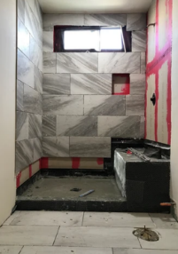Small tiled bathroom under renovation with a raised black shower base and a window near the ceiling