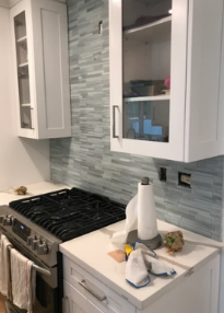 Modern white kitchen with gas stove, cabinets, and countertop tray on blue-gray tile backsplash