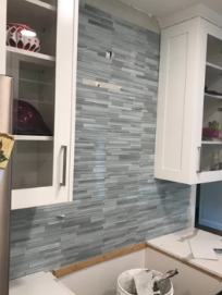 Kitchen backsplash with gray mosaic tile and white cabinets above a sink area
