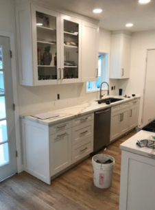 Bright modern kitchen with white cabinets, gray countertops, and a sink beside a dishwasher.
