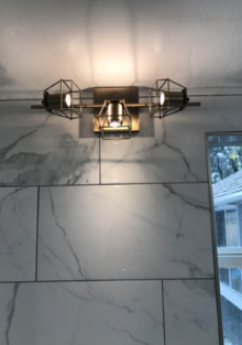 Modern wall sconce with black metal cages on a marble-tile wall above a window