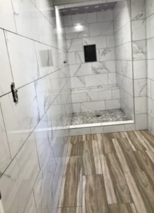 Marble-tiled walk-in shower with glass door and wood-look floor outside